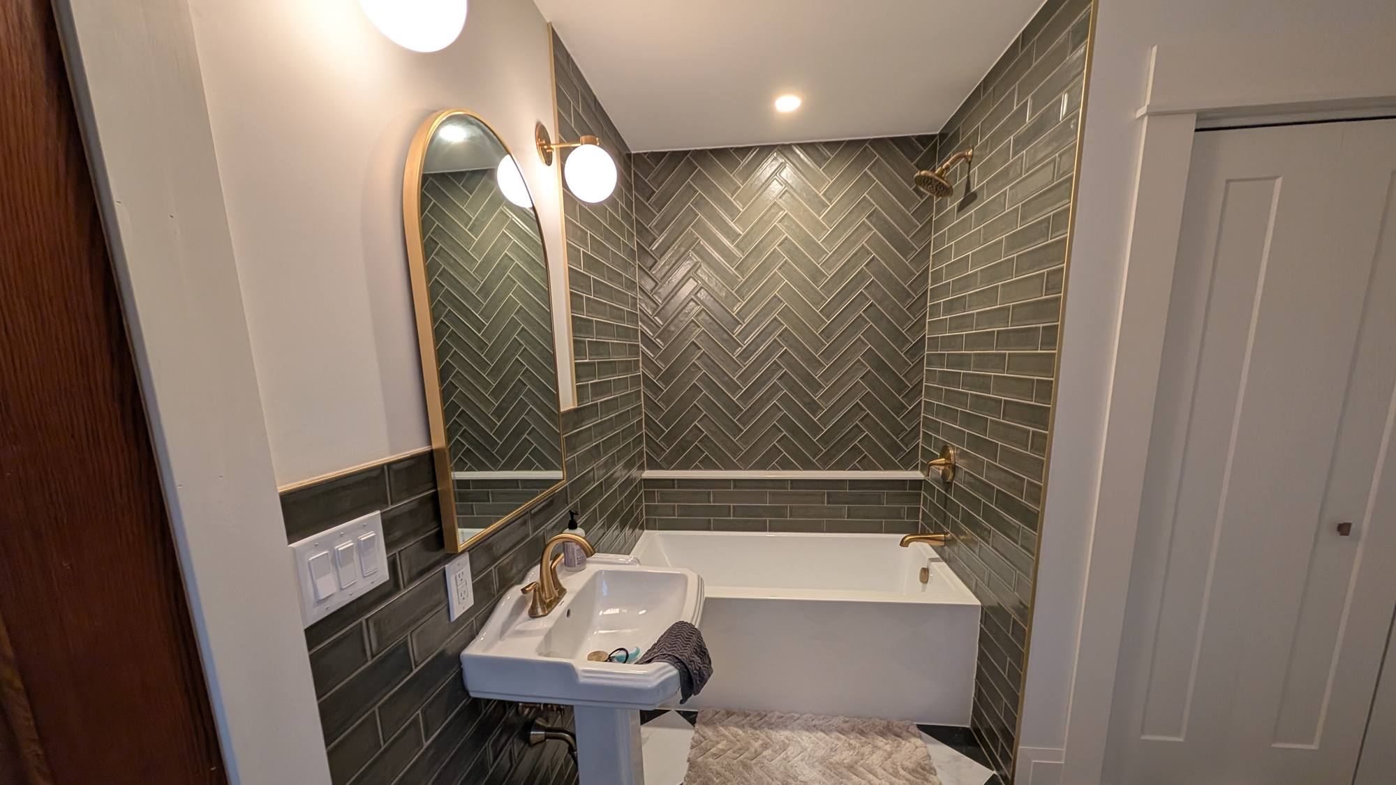Renovated bathroom with green herringbone tile and marble floor