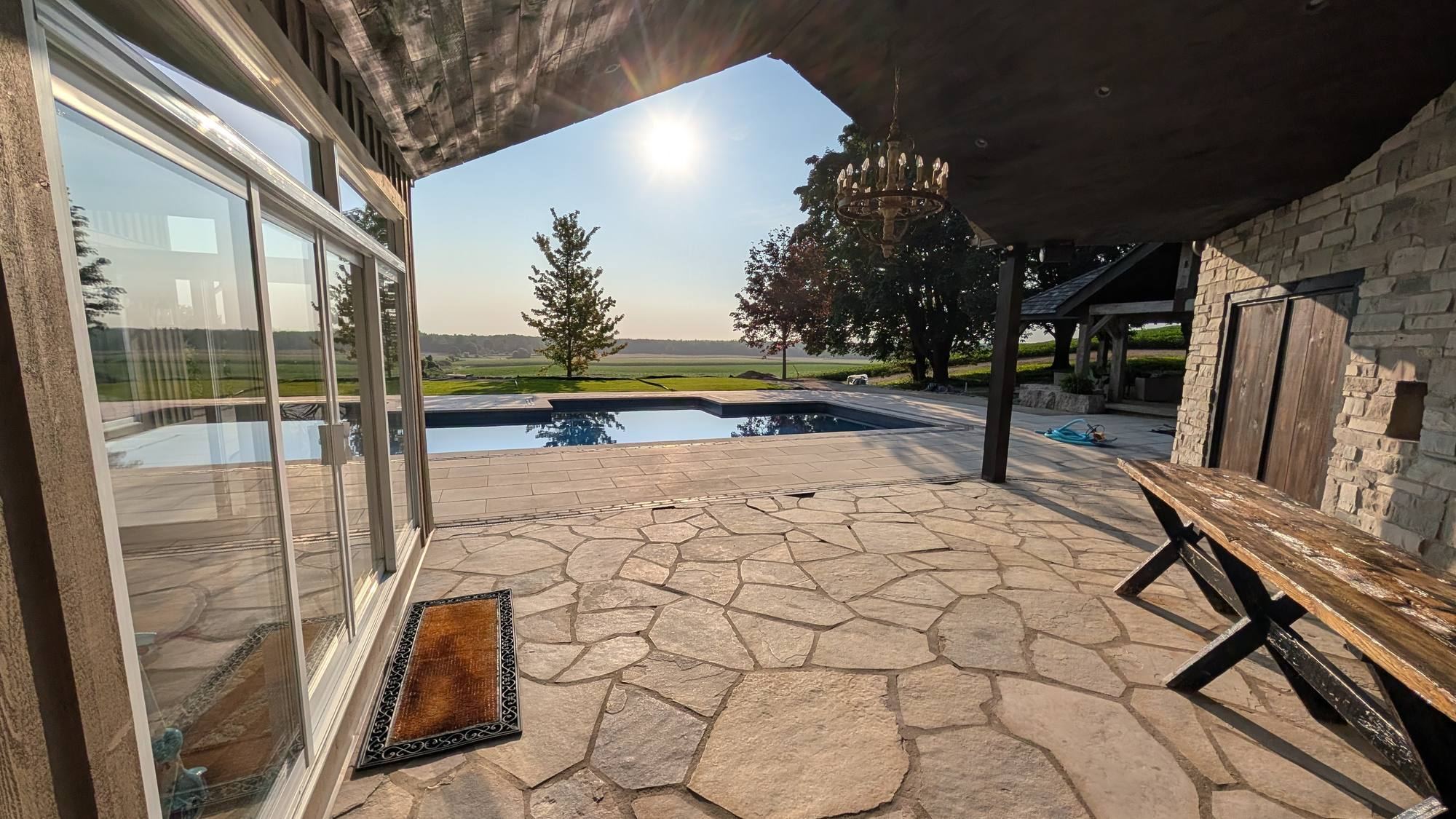Covered flagstone patio looking out to a pool and open field at sunset