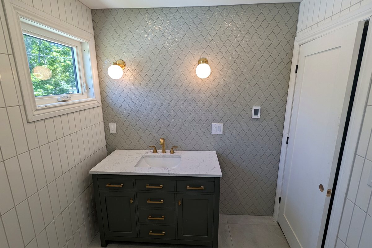 The same bathroom finished: scalloped tile across the vanity wall, brass sconces, a dark green vanity under a quartz top