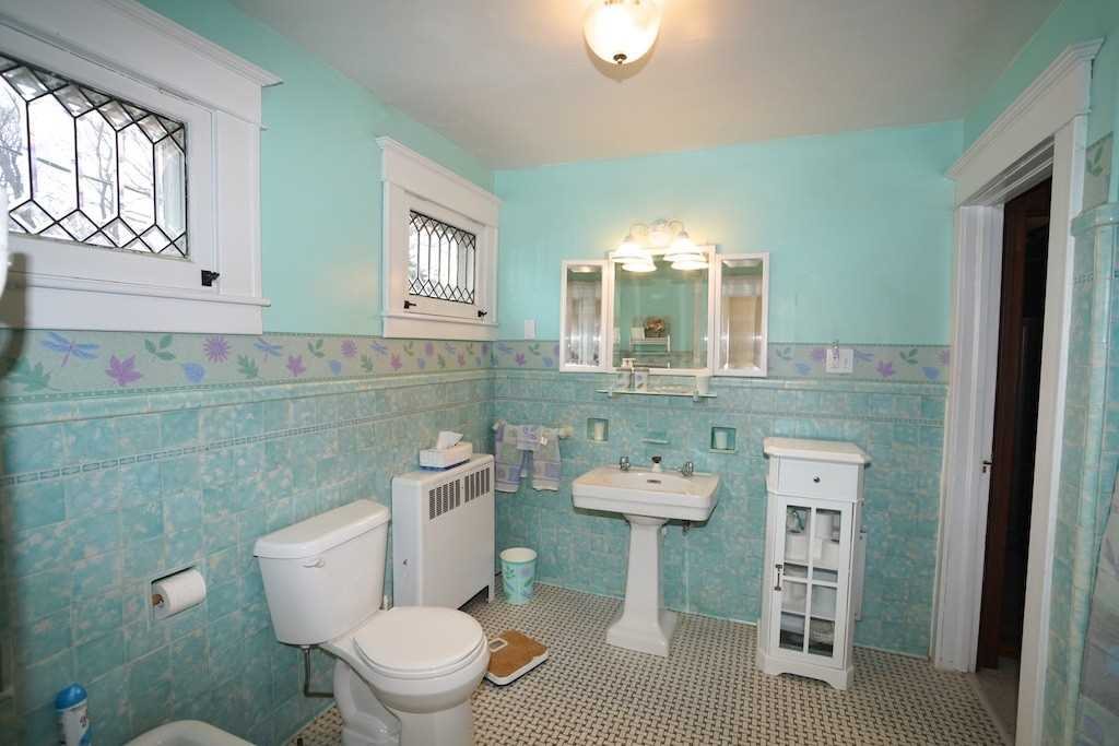 The original bathroom in a century home: turquoise wall tile with a painted border, a pedestal sink and a radiator